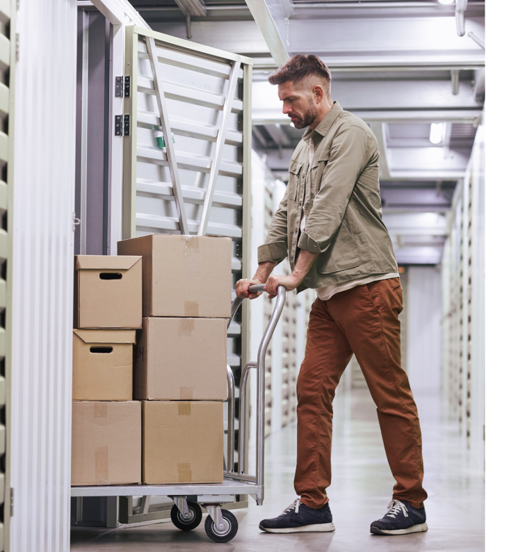 A man is pushing a trolley loaded with cardboard boxes into a storage unit.