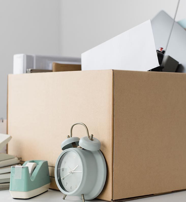 Desk items are packed in a storage box. An alarm clock & sellotape dispenser are placed in front.