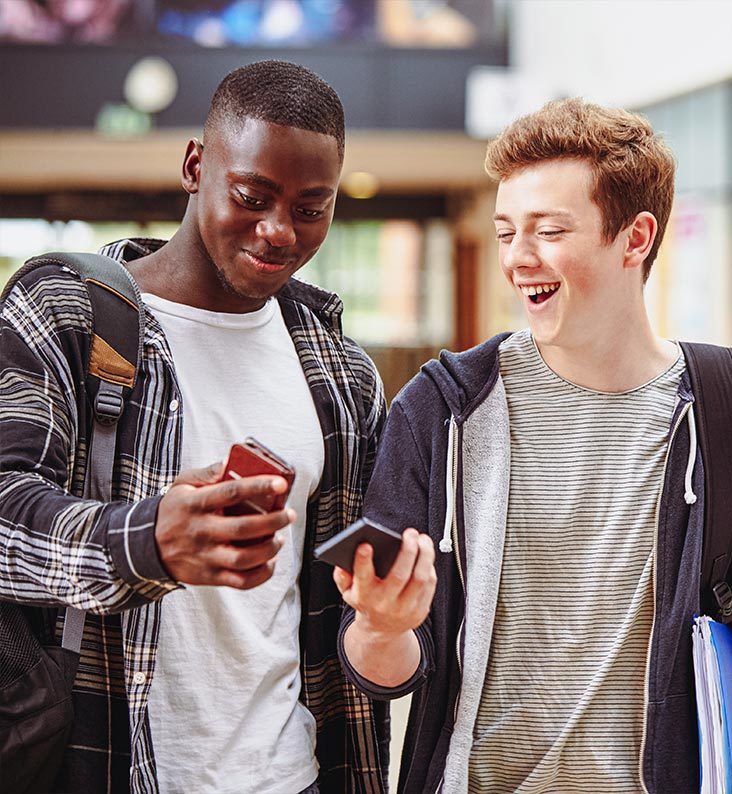 Two students are smiling down at a mobile phone.