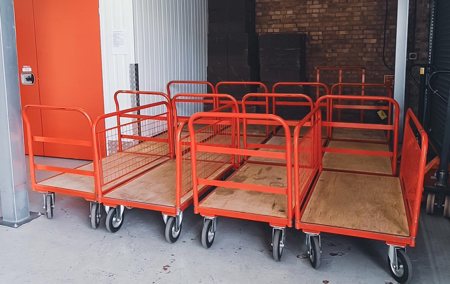 Three rows of red pallet trolleys are stored in a loading bay.