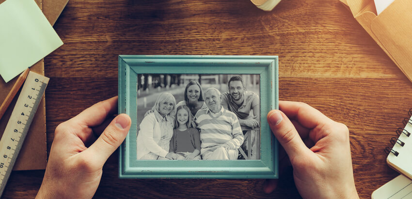 Image of hands holding a black and white colour family photo in a turquoise picture frame.