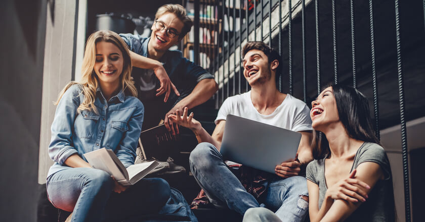 Image of students laughing together holding books and a laptop.
