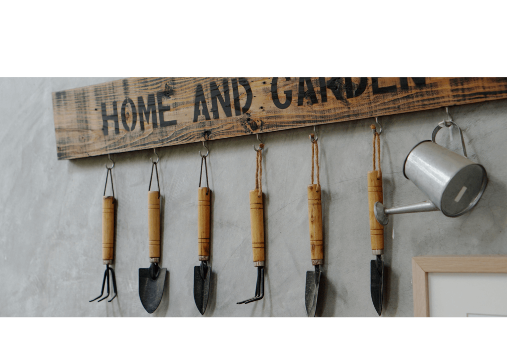 Garden tools hanging on a wooden sign on a wall that's embossed with the text 'HOME AND GARDEN'.