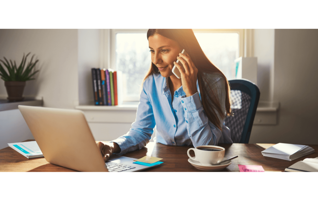 A woman on the phone at her laptop with a coffee working from home.