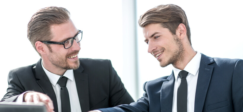 Image of 2 men working together in work suits smiling. 