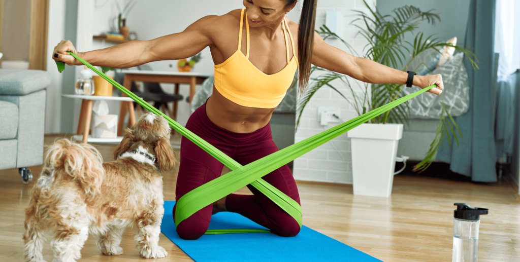 A woman exercising at home with a resistance band with her small dog watching.