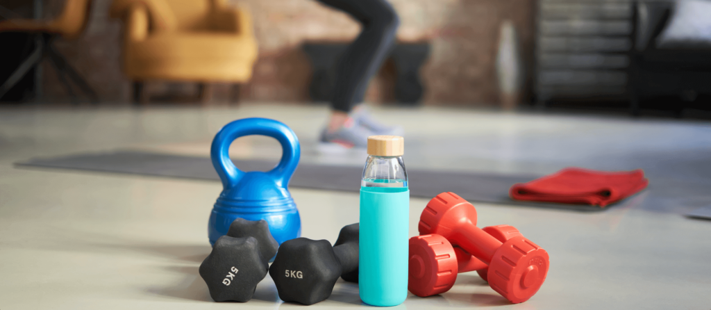A kettle bell, four weights and a water bottle on the floor of a home gym.