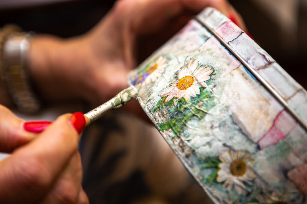 A close up image of somebody handpainting a memory box with flowers.